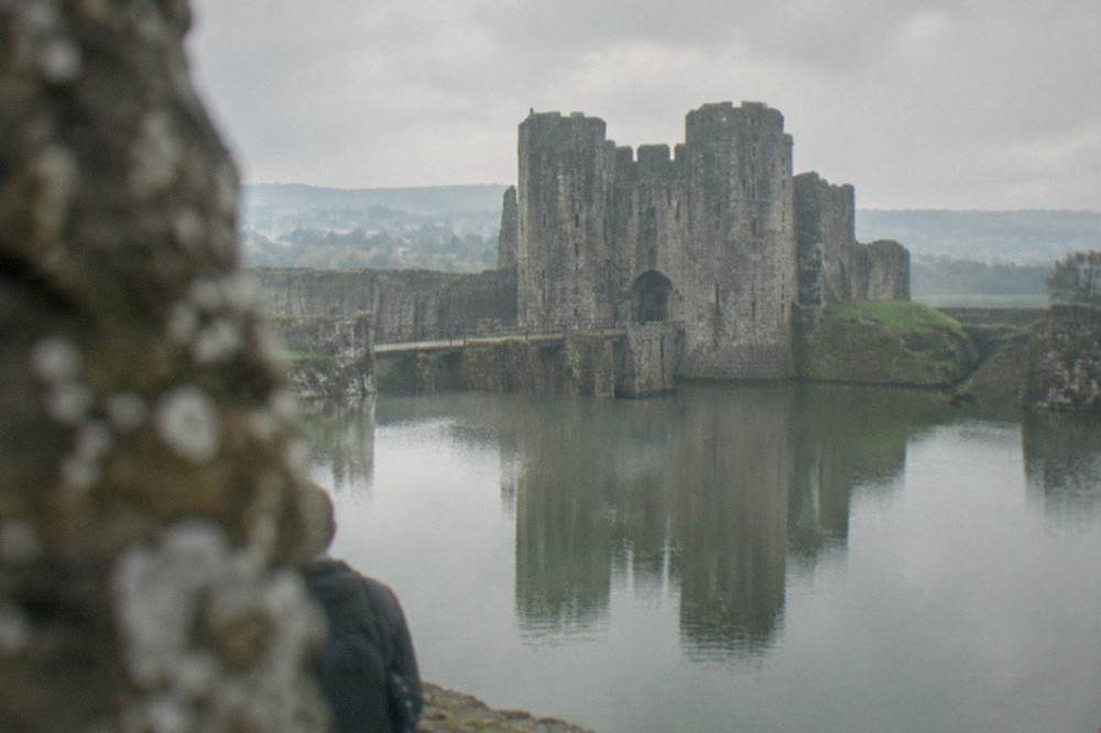 A stone castle with twin towers reflected in a wide moat under morning light