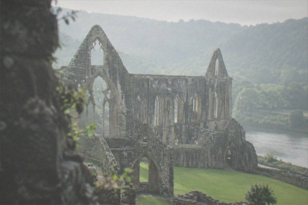 A ruined abbey with tall gothic arches standing in a green river valley