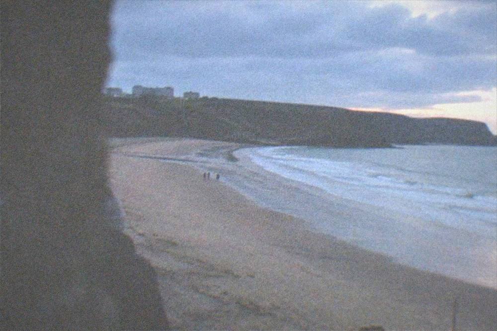 A long sandy beach curving between cliffs with waves rolling onto the shore