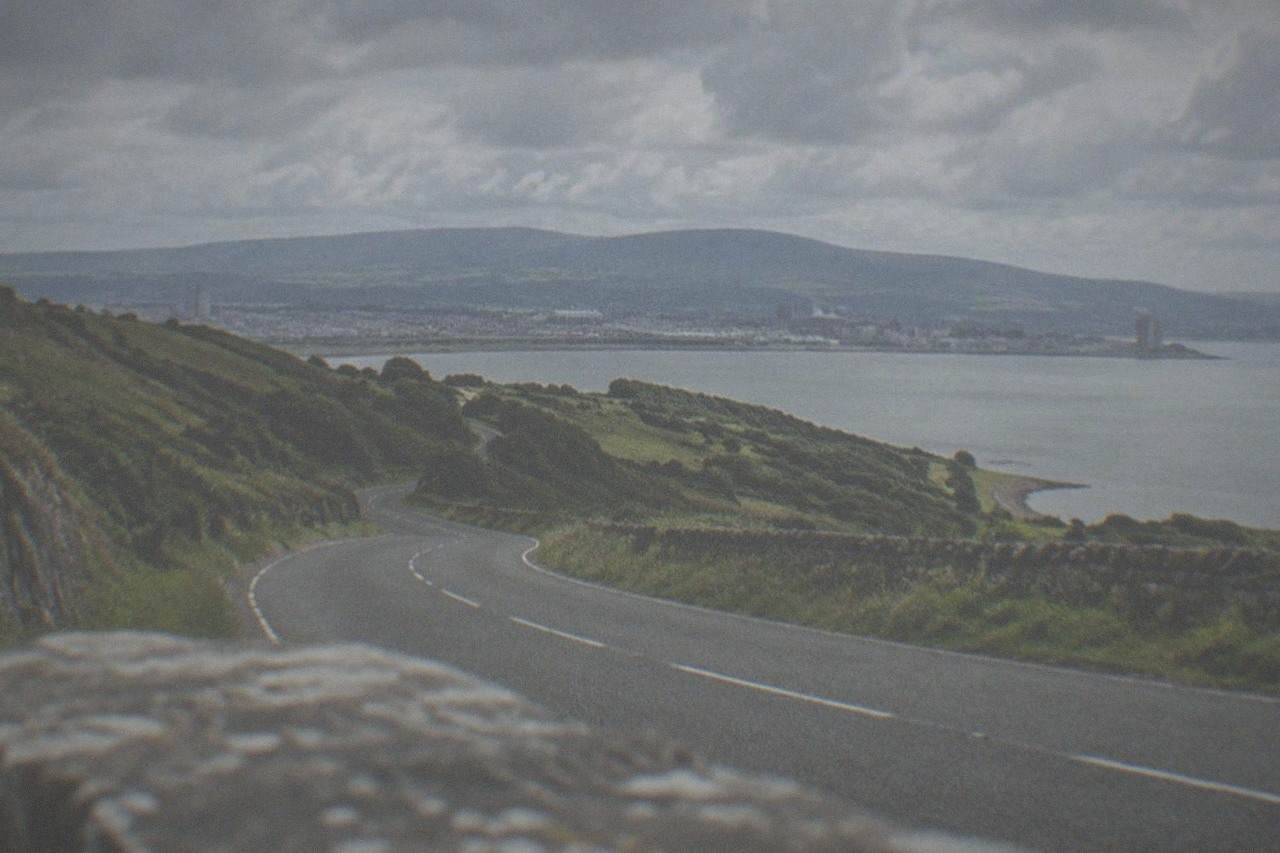 A winding road through green hills with distant mountain ridges under a wide sky
