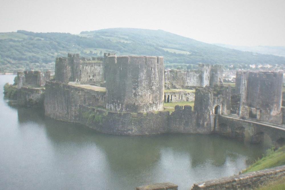 A stone castle rising above a lake with green hills behind