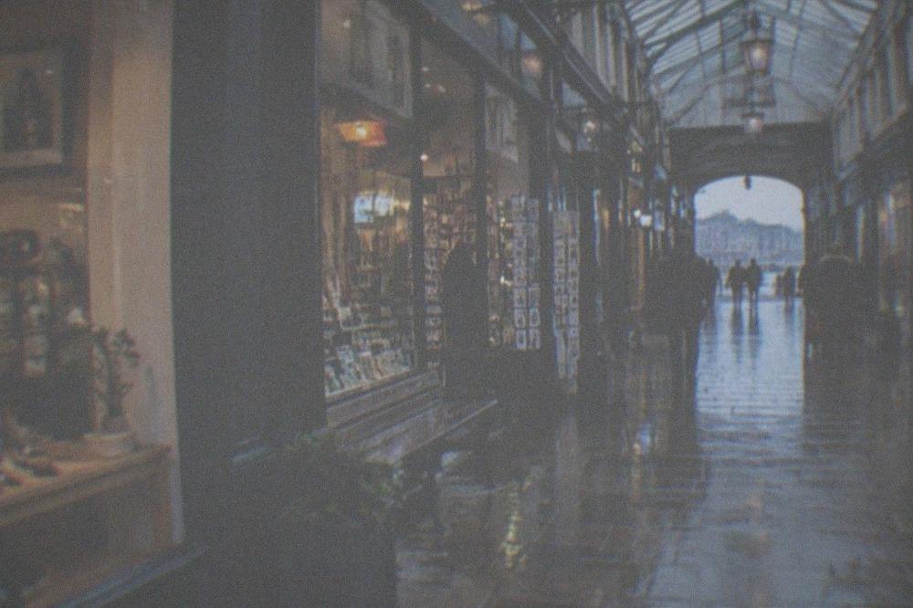 A covered Victorian shopping arcade lit by shopfronts on a wet day
